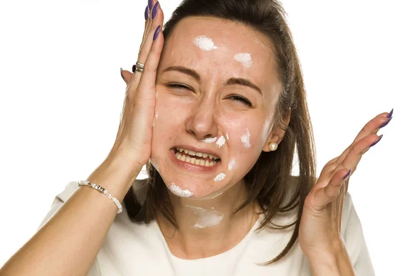 怒っていると不幸な女性は白い背景に顔クリームを適用 — ストック写真