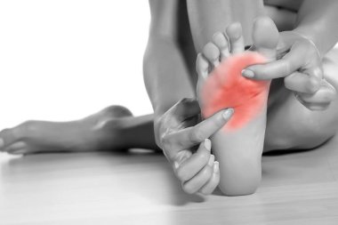 Beyaz arka planda acılı ayağına masaj yapan bir kadın.