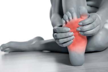 Beyaz arka planda acılı ayağına masaj yapan bir kadın.