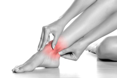 Kadın beyaz arka planda ağrılı ayak bileğine masaj yapıyor.