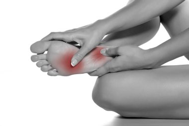 Beyaz arka planda acılı ayağına masaj yapan bir kadın.