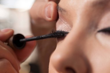 Makyaj sanatçısı müşterinin gözüne rimel sürmüş.