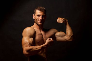 Yarı çıplak, yakışıklı ve kaslı genç adam koyu bir arka planda poz veriyor.