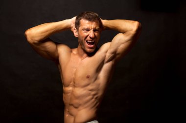 Yarı çıplak, yakışıklı ve kaslı genç adam koyu bir arka planda poz veriyor.