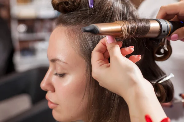 A hairdresser makes curls with a iron and hair clips