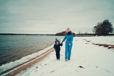 Annesi kışın gölün kumsalında el ele tutuşan mutlu bir çocuk. 