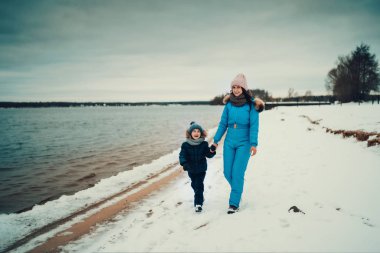 Anne ve oğullarının el ele tutuşup kışın göl kenarında yürüdükleri gün ışığı. 