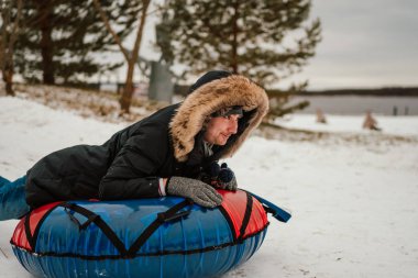 Genç adam eğlence için tüp topuz kullanıyor, kışın tepeden aşağı at sürüyor. 