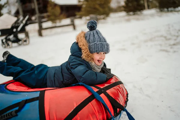 ワイヤーパークで雪のチューブそりを膨らませてカメラを見て笑っている男の子 — ストック写真