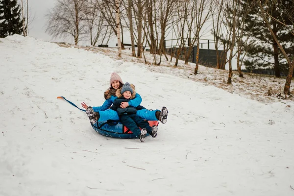 かわいい男の子と彼の母親は冬にインフレータブル雪チューブで丘を下り — ストック写真