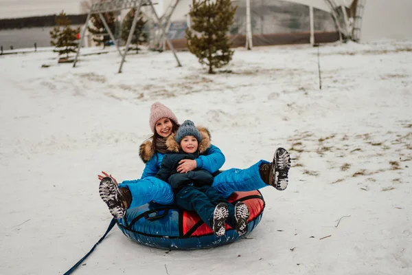 暖かい服を着た母親と息子が一緒に冬の楽しみのためにチューブパンを使用して — ストック写真