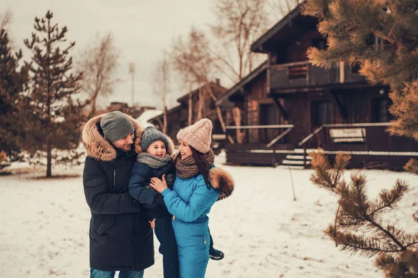 Mutlu anne ve baba oğullarını ellerinden tutar ve kışın dışarıda gülerler.