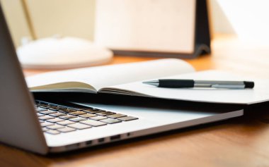 Modern Ahşap İşletme Masasında Odaklanmamış Arkaplanda Not Defteri ve Kalemi olan Dizüstü Bilgisayar.