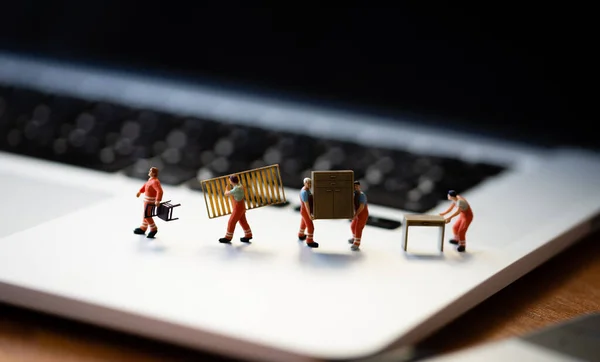 Miniatures of figurines workers moving furniture with keyboard at background.