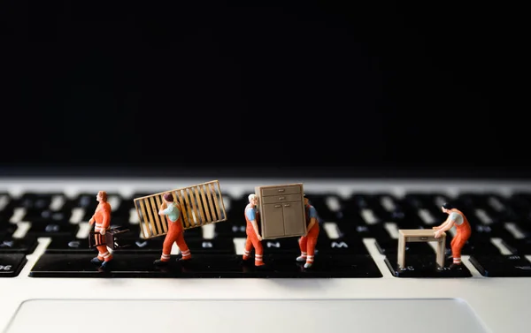 Miniatures of figurines workers moving furniture with keyboard at background.