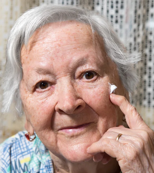 Mulher velha aplicando creme anti-envelhecimento — Fotografia de Stock