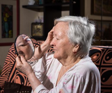 Yaşlı kadın bir aynaya bakıyor 