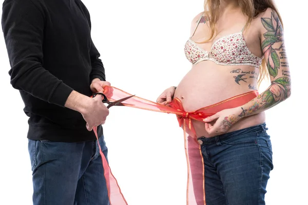 Terhes nő hasa pózol a férjem körül piros szalaggal — Stock Fotó