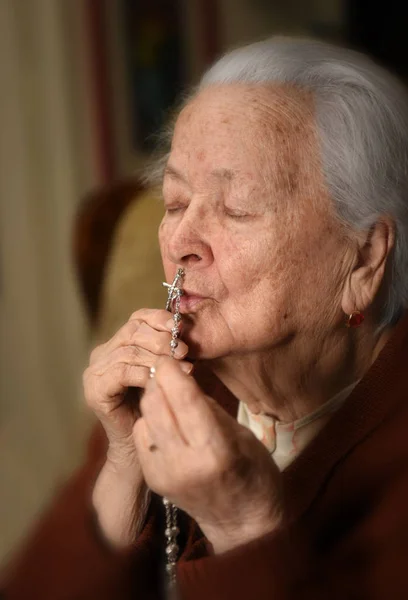 Old woman praying and  holding silver rosary — Stock Photo, Image