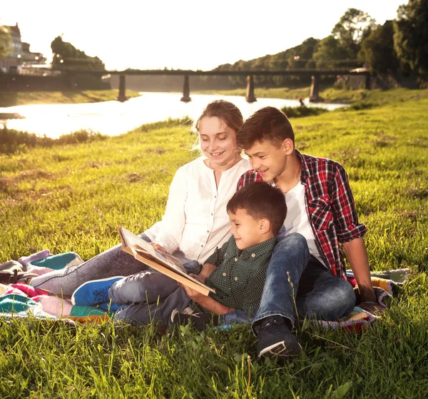 Niños sentados en la hierba y leyendo el libro — Foto de Stock