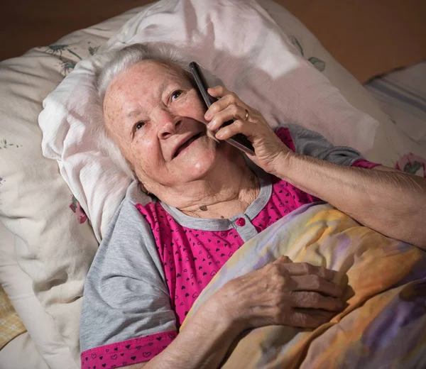 Vecchia malata sdraiata a letto e utilizzando lo smartphone — Foto Stock