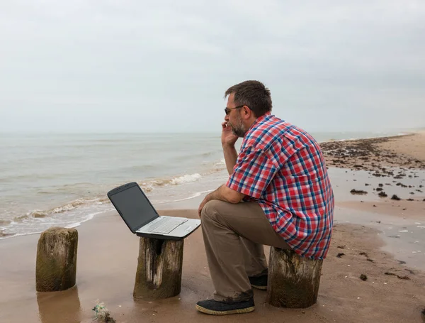 Homme âgé assis à la plage avec ordinateur portable — Photo