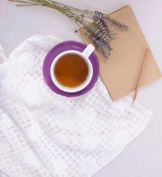 A cup of tea, lavender and notebook with pencil on a light backg