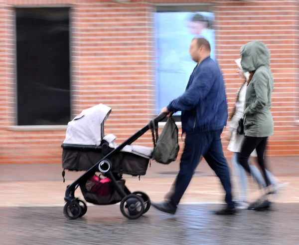 Familia con un niño pequeño en el cochecito caminando por la calle —  Fotos de Stock