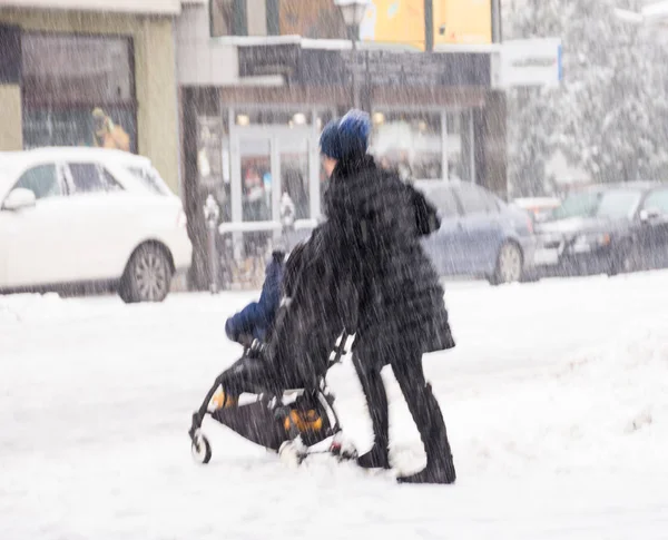 Mutter geht bei verschneitem Wintertag mit Kind im Kinderwagen. — Stockfoto
