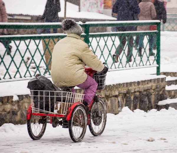 Kvinna rida en trehjuling på gatan i staden i vinter snö — Stockfoto