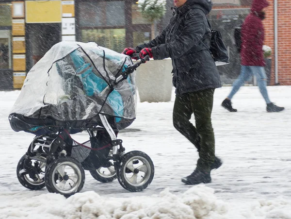 Mutter geht bei verschneitem Wintertag mit Kind im Kinderwagen. — Stockfoto