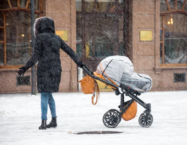 母は雪の冬の日にベビーカーで子供と歩く. — ストック写真