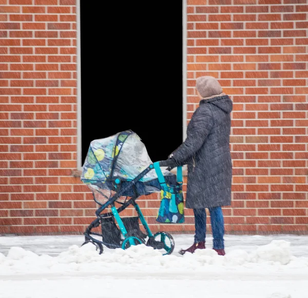 Madre camina con el niño en el cochecito en el día de invierno nevado . —  Fotos de Stock