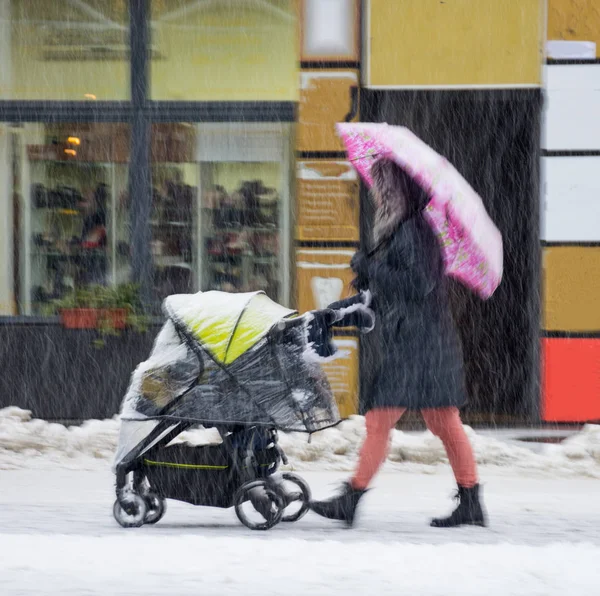 Madre camina con el niño en el cochecito en el día de invierno nevado . —  Fotos de Stock