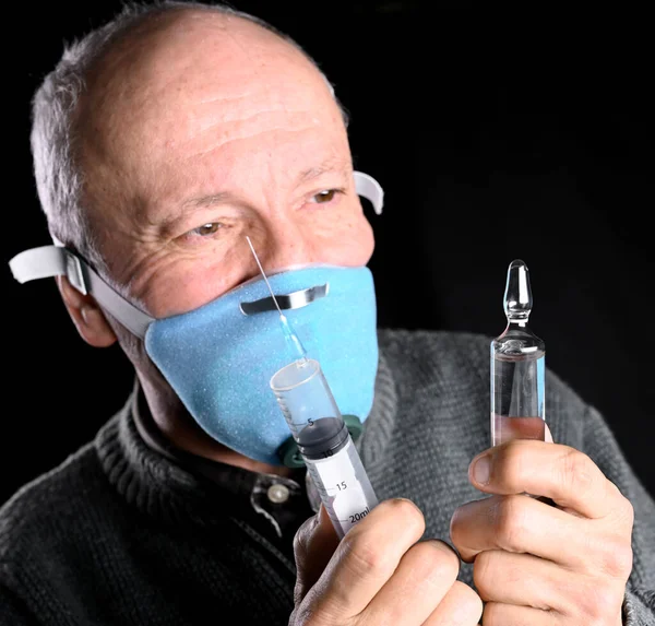 Homme âgé en masque tenant seringue et ampoule sur fond noir — Photo