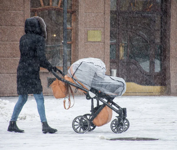 Anne, bebekle birlikte karlı kış arabasında yürüyor. — Stok fotoğraf