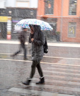 Yağmurlu günde sokakta şemsiyeli bir kadın yürüyor. Kasıtlı hareket bulanıklığı. Defokus görüntüsü