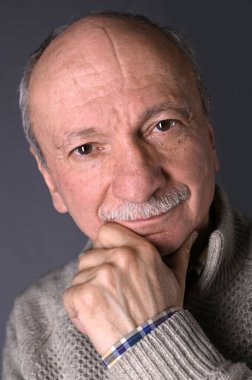 Karanlık bir arka planda gülümseyen yaşlı adamın portresi.