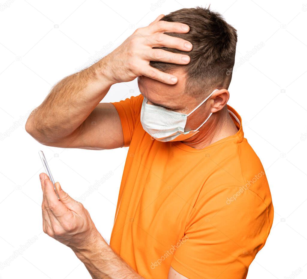 Healthcare and medical concept. Man in mask holding thermometer in hands, measuring body temperature while suffering from influenza. Frustrated male with thermometer feeling sick