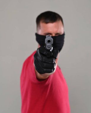 Stüdyoda gri arka planda duran siyah maskeli bir adam.