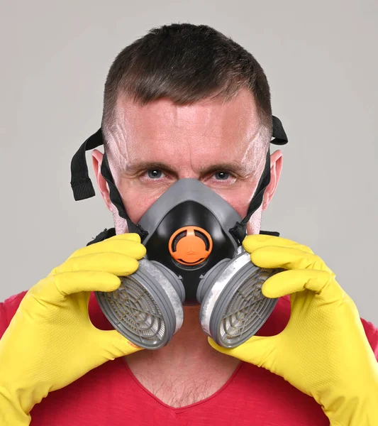 Coronavirus and healthcare concept. Respiratory protection. Portrait of young man in gloves wearing respirator over gray background