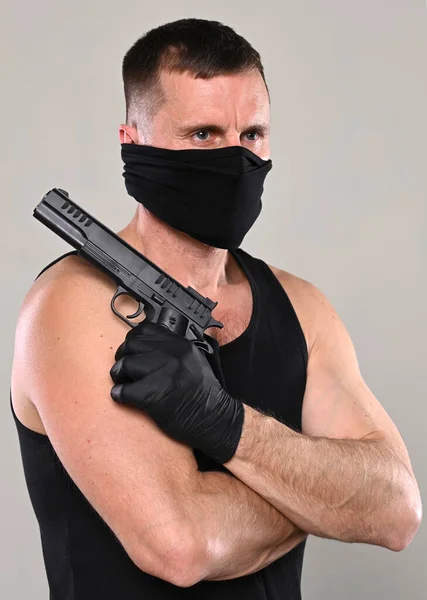 带着黑色面具的男人 带着枪在灰色背景的工作室里摆姿势 — 图库照片