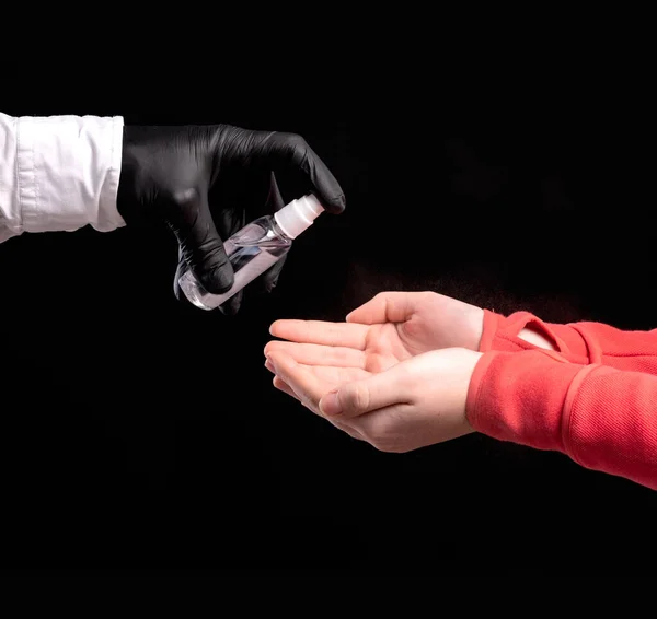 戴黑色防护手套的医生在黑色背景上用防腐剂治疗病人的双手 — 图库照片