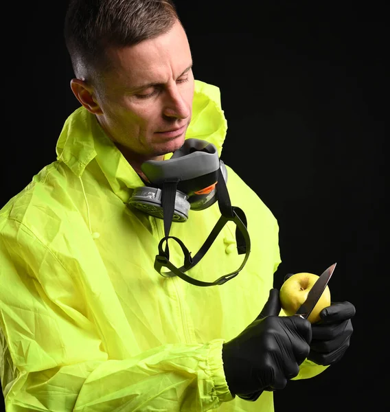 Man with respirator and in protective gloves cutiing an apple over black background