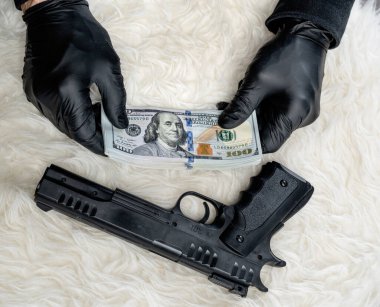 Silahın yakın görüntüsü ve eldivenli soyguncunun elinde dolar var.