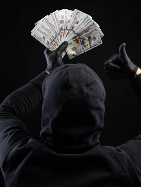 İş ve finans kavramı. Siyah kapüşonlu adam siyah arka planda Amerikan doları taşıyor.