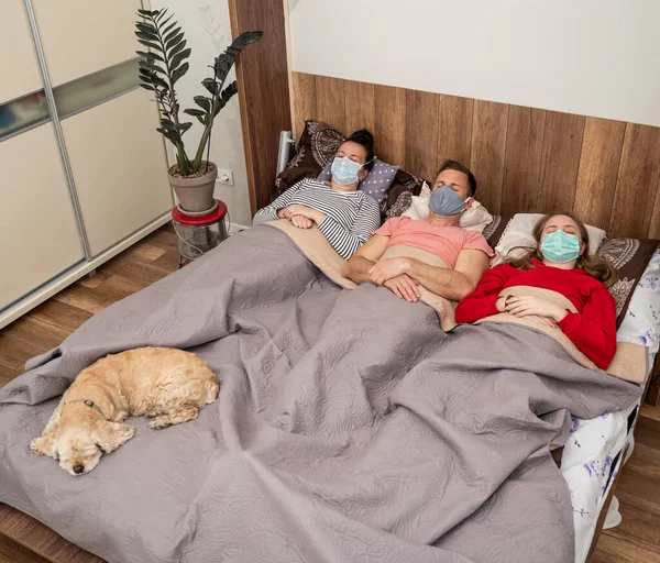 Healthcare concept. Sick family in protective masks  lying in bed at home