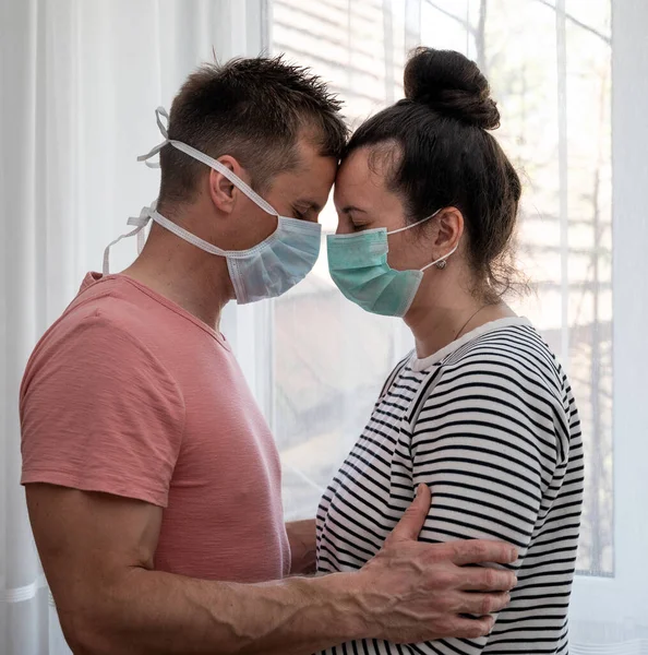 Healthcare concept. Sad couple in masks posing near window at home