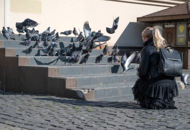 UZHOROD, UKRAINE - 10 Nisan 2020: Ukrayna 'nın Ukrayna şehir merkezindeki meydanda güvercinleri besleyen genç kadın