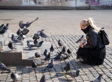UZHOROD, UKRAINE - 10 Nisan 2020: Ukrayna 'nın Ukrayna şehir merkezindeki meydanda güvercinleri besleyen genç kadın